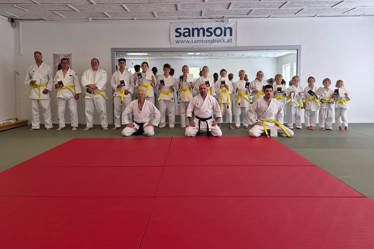Gruppenfoto nach der Gürtelprüfung: Kinder und Erwachsene im Karateanzug zeigen ihre Urkunden im Dojo
